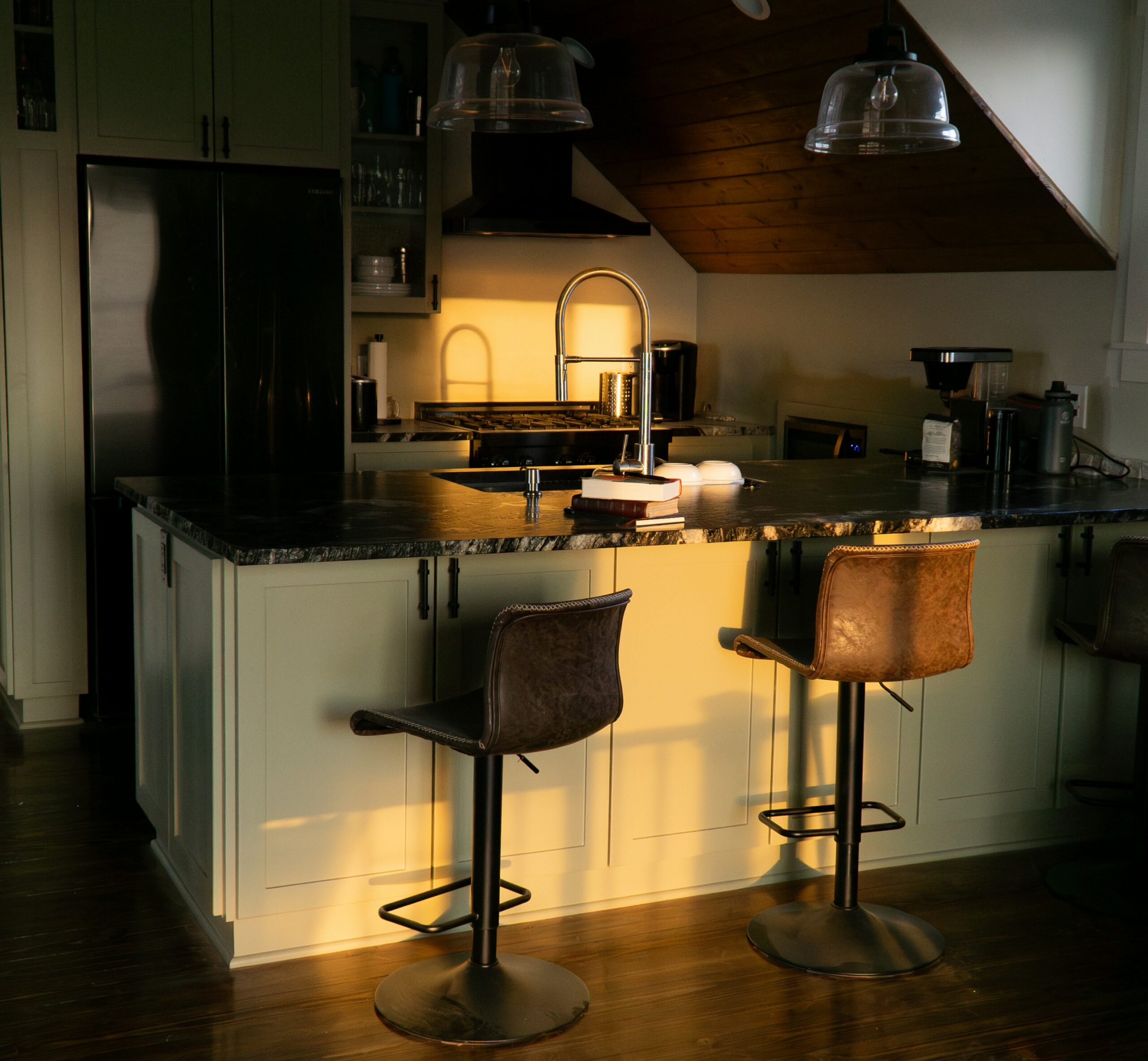 A couple of stools that are in a kitchen, while the sunlight iluminates part of the kitchen